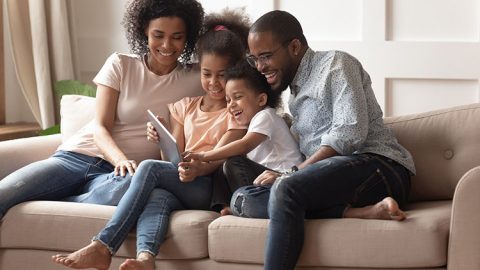 Happy black parents and children using digital tablet on sofa