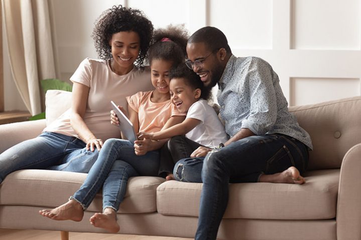 Happy black parents and children using digital tablet on sofa