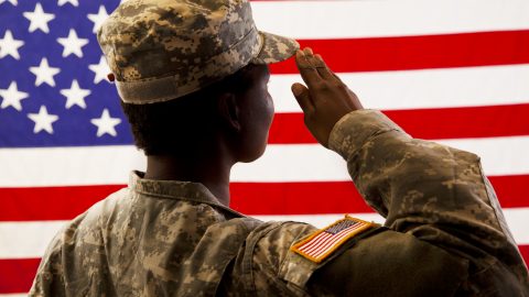 African American military woman salutes USA flag.