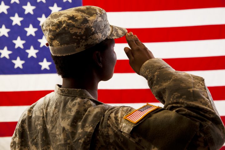 African American military woman salutes USA flag.