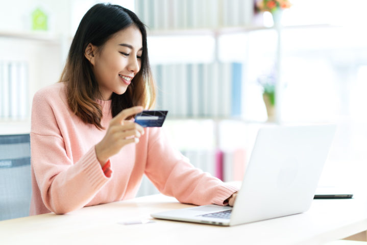 Young attractive asian woman holding credit card sitting at table typing keyboard on laptop computer to shopping online at home office or library. Happy girl student buy and pay in ecommerce concept.