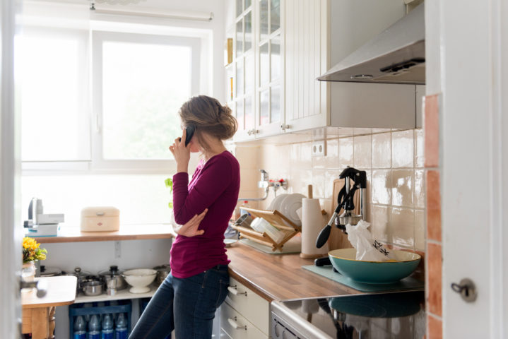 A young woman standing at home in her kitchen while making a telephone call